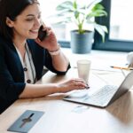 Woman smiling and talking on phone while working on laptop