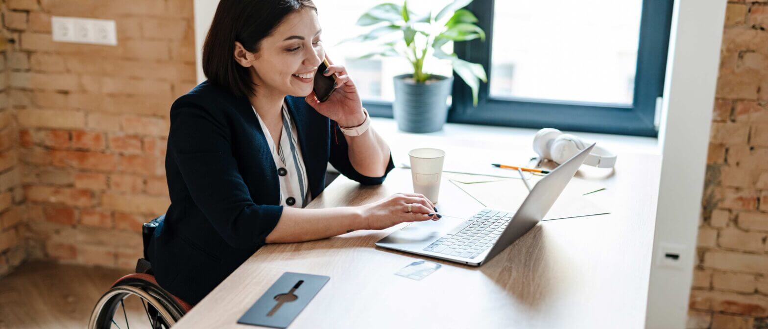 Woman smiling and talking on phone while working on laptop